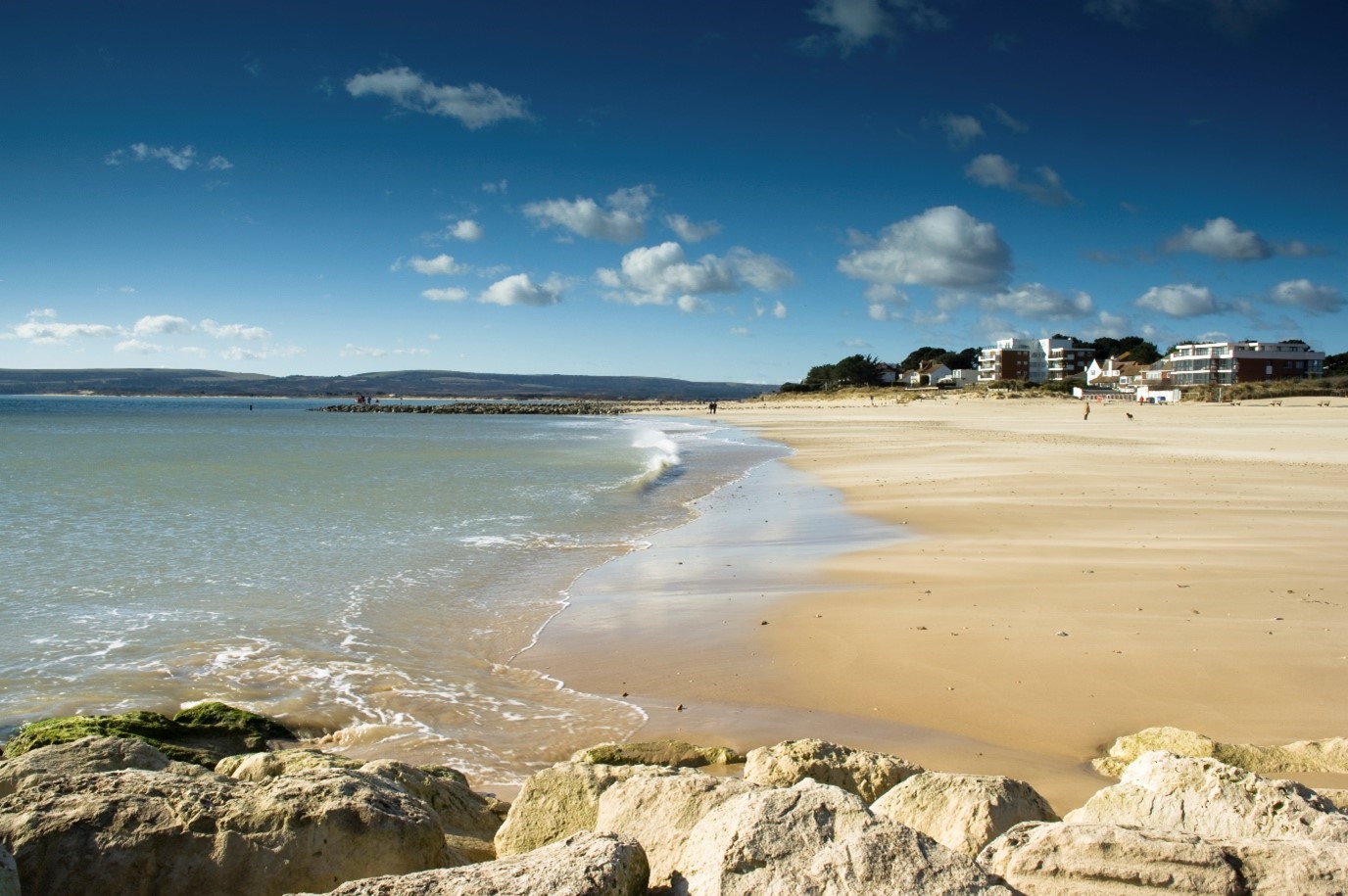 Sandbanks beach with the sand and sea in shot and buildings in the background with clouds in the sky