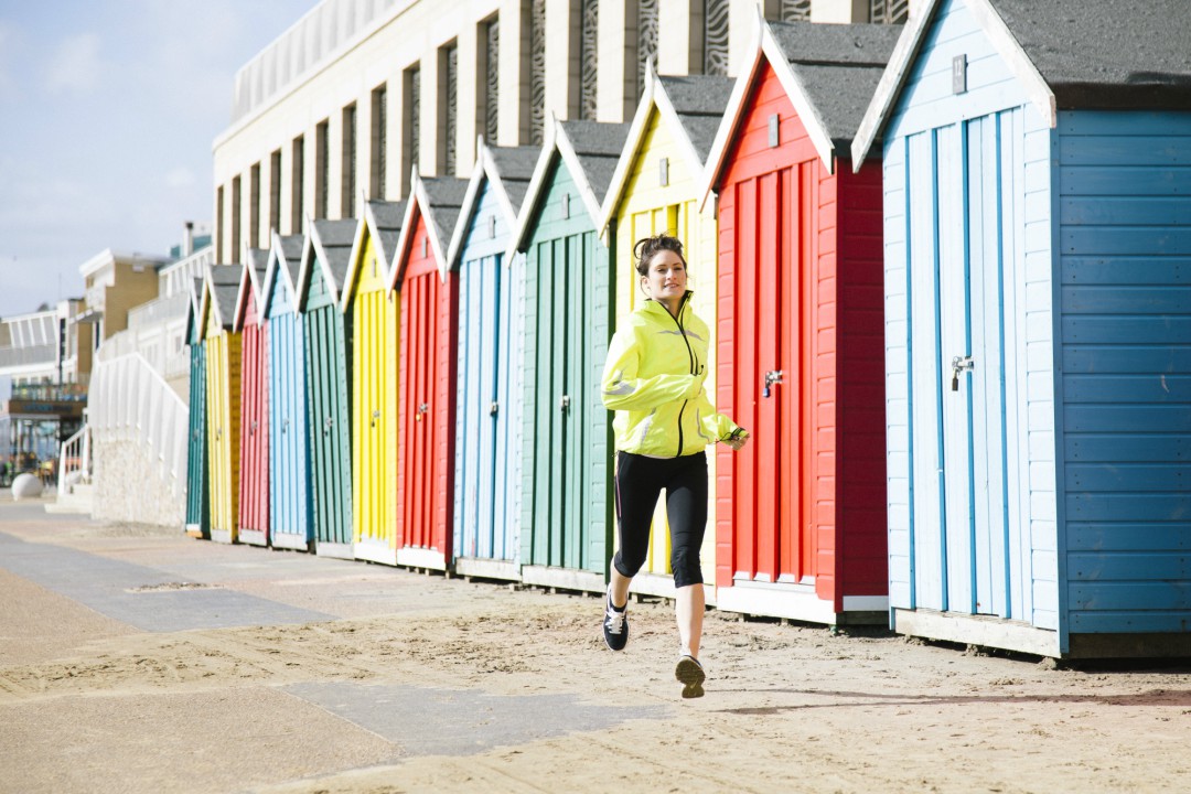 A woman in a high-vis yellow jacket running alongside a sunny Bournemouth seafront